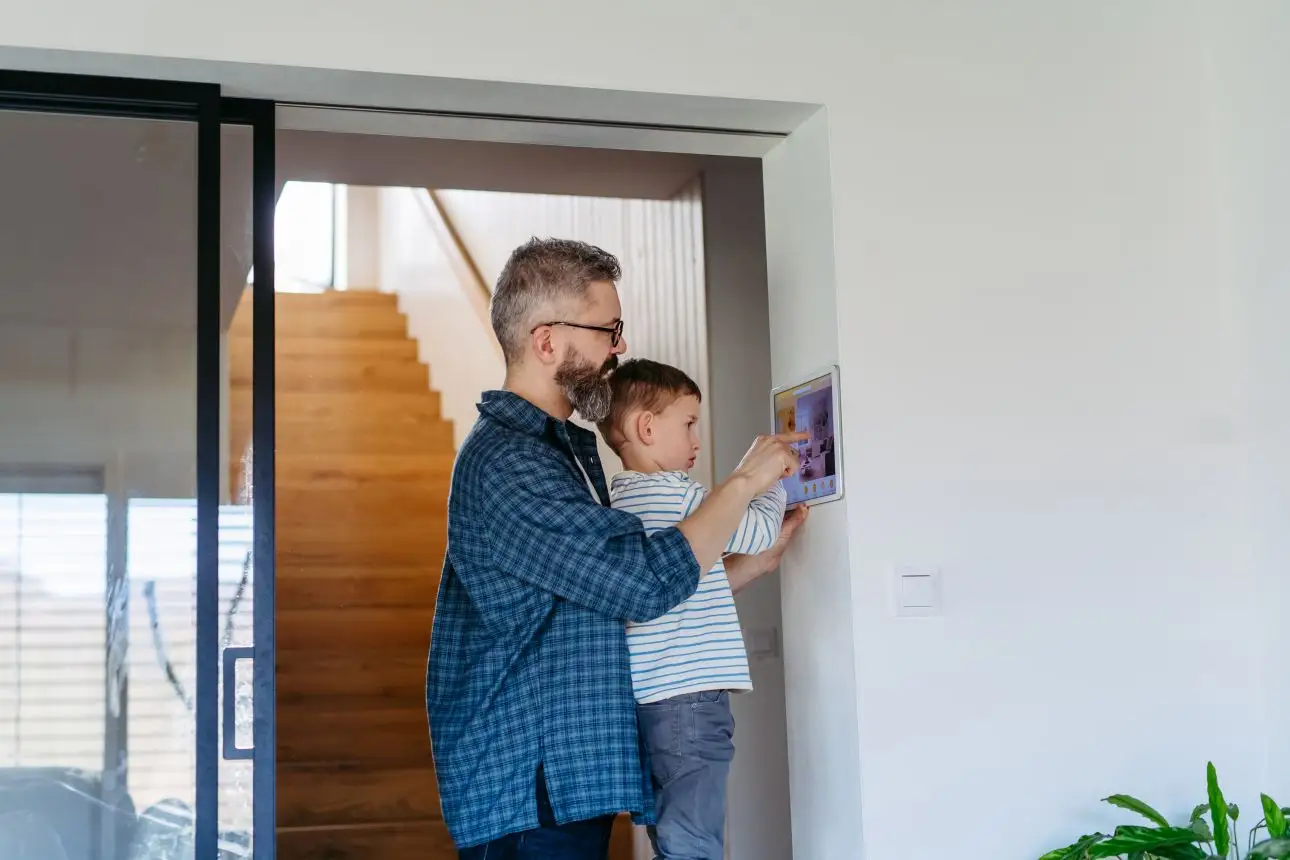 Father holding his young son while using a home energy management system. . 